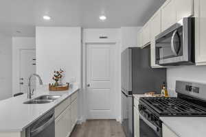 Kitchen with stainless steel appliances, a peninsula, light wood-style flooring, light stone counters, and recessed lighting