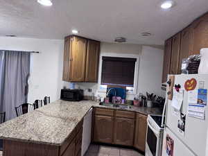Kitchen with white appliances, a textured ceiling, light stone countertops, a peninsula, and light tile patterned flooring