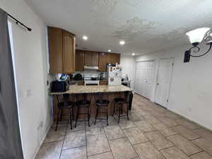 Kitchen with a breakfast bar, a peninsula, white appliances, a textured ceiling, and light stone countertops
