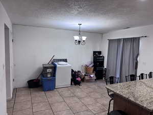 Dining area with washer / dryer, a chandelier, a textured ceiling, and light tile patterned floors