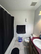 Bathroom with tile patterned floors, vanity, shower / bathtub combination with curtain, and a textured ceiling