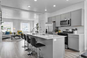 Kitchen with gray cabinets, appliances with stainless steel finishes, a kitchen bar, a center island with sink, and recessed lighting