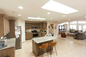Kitchen with open floor plan, arched walkways, stainless steel appliances, a kitchen bar, and light stone countertops