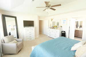 Bedroom featuring ensuite bath, light carpet, ceiling fan, and a tray ceiling