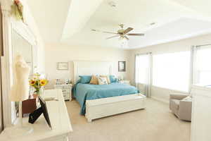 Bedroom with a tray ceiling, light carpet, and ceiling fan