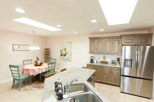 Kitchen featuring a skylight, stainless steel appliances, recessed lighting, light stone counters, and pendant lighting