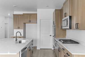 Kitchen featuring light stone countertops, light wood finished floors, stainless steel appliances, a textured ceiling, and an island with sink