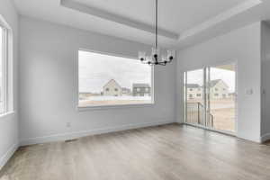 Unfurnished dining area featuring a tray ceiling, a chandelier, and light wood-style floors