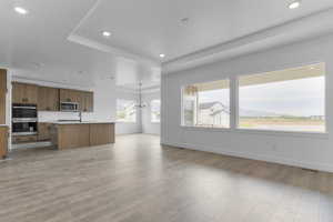 Unfurnished living room featuring recessed lighting, a raised ceiling, light wood-style flooring, and a chandelier