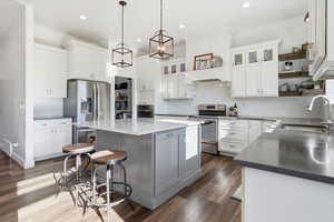 Kitchen with tasteful tile backsplash, glass insert cabinets, open shelves, gray island cabinetry, pendant and recessed lighting