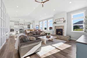 Living room with lofted ceiling, a stone fireplace, wall with box molding, dark wood finished floors, recessed lighting, and ceiling fan