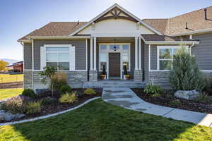 View of front of house featuring stone siding, a porch, a front yard, and roof with shingles