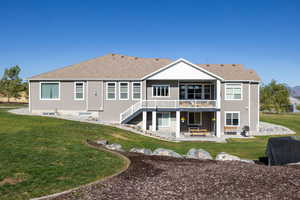 Rear view of property with a covered deck, patio, a lawn, stairs, and a shingled roof
