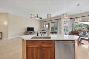 Kitchen featuring hanging light fixtures, a kitchen island with sink, stainless steel dishwasher, brown cabinetry, and open floor plan