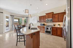 Kitchen with brown cabinetry, tasteful backsplash, stainless steel appliances, decorative light fixtures, and a kitchen island with sink