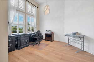 Home office featuring a towering ceiling, light wood-type flooring, and a chandelier