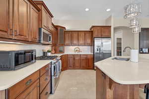 Kitchen with brown cabinets, stainless steel appliances, decorative backsplash, glass insert cabinets, and hanging light fixtures