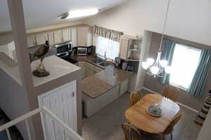 Kitchen featuring hanging light fixtures, open shelves, vaulted ceiling, dark stone countertops, and stainless steel microwave