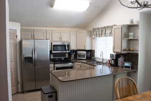Kitchen featuring appliances with stainless steel finishes, dark stone countertops, lofted ceiling, open shelves, and a peninsula