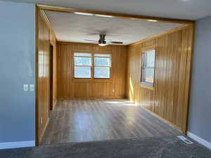 Empty room featuring ceiling fan, dark wood finished floors, wood walls, crown molding, and dark carpet