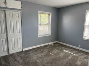 Unfurnished bedroom featuring dark colored carpet, a textured ceiling, and a closet