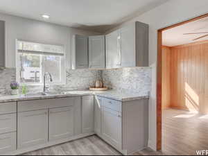 Kitchen with light wood-type flooring, light stone counters, tasteful backsplash, white cabinetry, and ceiling fan