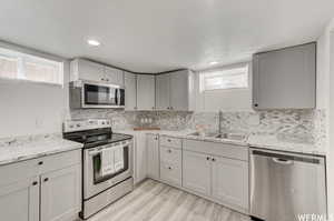 Kitchen featuring stainless steel appliances, gray cabinets, decorative backsplash, and light wood finished floors