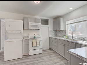 Kitchen featuring white appliances, light countertops, light wood-style flooring, stacked washer and clothes dryer, and decorative backsplash