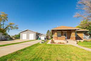 View of front of house with a front lawn, covered porch, brick siding, an outbuilding, and a detached garage