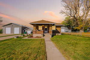 View of front of home with brick siding, a shingled roof, a garage, an outbuilding, and a porch