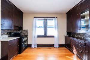 Kitchen with tasteful backsplash, dark brown cabinets, double oven range, and light wood-style floors
