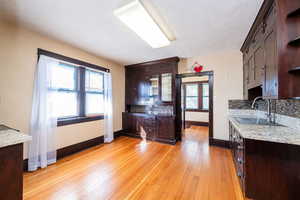 Kitchen featuring dark brown cabinets, decorative backsplash, light stone countertops, light wood-style flooring, and glass insert cabinets
