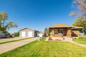 View of front of house featuring a front yard, brick siding, a porch, an outdoor structure, and roof with shingles