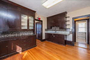 Kitchen with dark brown cabinets, light wood-style floors, tasteful backsplash, a textured ceiling, and open shelves