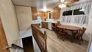 Kitchen with light countertops, light wood finished floors, brown cabinetry, white appliances, and a ceiling fan