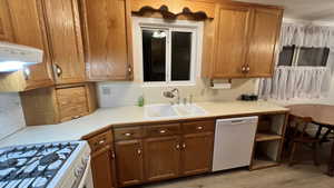 Kitchen with light countertops, white appliances, brown cabinetry, light wood-style flooring, and ventilation hood