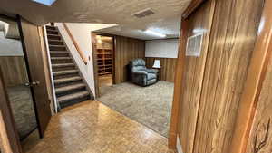 Living area with wood walls, stairs, a textured ceiling, and light colored carpet