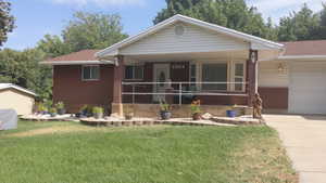 View of front of house featuring a front lawn, a porch, roof with shingles, and an attached garage