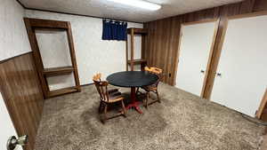 Carpeted dining space featuring wood walls and a textured ceiling