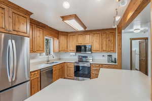 Kitchen with stainless steel appliances, brown cabinetry, and pendant lighting