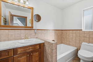 Full bath with a bath, tile walls, vanity, and wainscoting