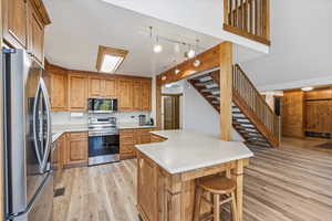 Kitchen featuring stainless steel appliances, light countertops, brown cabinetry, light wood finished floors, and a center island