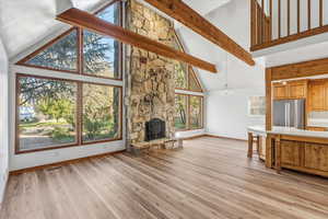 Unfurnished living room featuring high vaulted ceiling, beam ceiling, a stone fireplace, and light wood finished floors