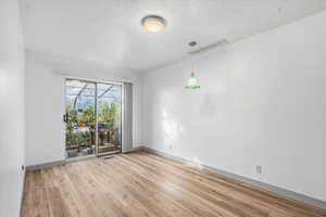 Spare room with a sunroom, light wood-style floors, and a textured ceiling