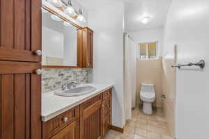 Full bath with light tile patterned floors, vanity, curtained shower, tasteful backsplash, and tile walls