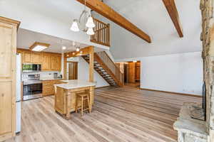 Kitchen featuring stainless steel appliances, light countertops, hanging light fixtures, beam ceiling, and open floor plan