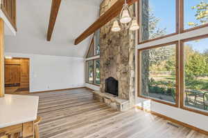 Unfurnished living room featuring high vaulted ceiling, wood finished floors, beam ceiling, a stone fireplace, and a chandelier