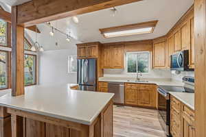 Kitchen with stainless steel appliances, decorative light fixtures, light wood-style floors, light countertops, and a center island