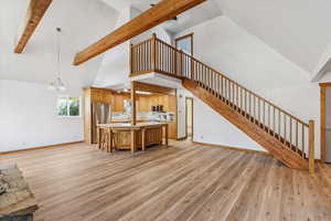 Kitchen with high vaulted ceiling, beam ceiling, light countertops, light wood-style flooring, and a kitchen island