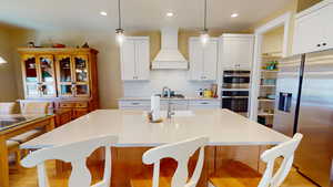 Kitchen featuring two toned cabinets, an island, a range hood, stainless steel appliances, and tile backsplash